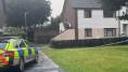 A police car sits beside police tape in front of a house 